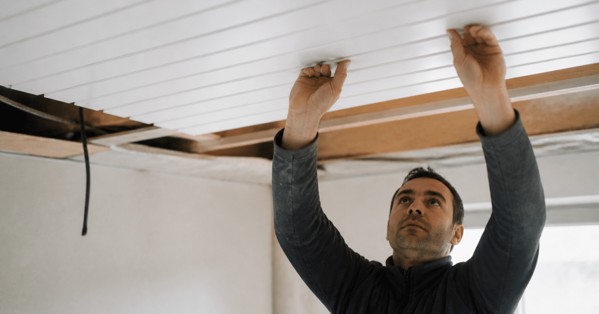 Ouvrier fixant panneaux plastiques blancs horizontalement au plafond