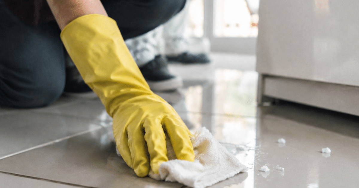 Main gantée essuyant residus blancs sur carrelage brillant