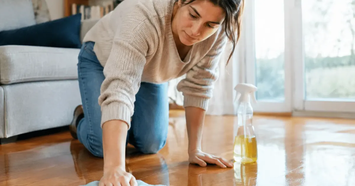 Personne agenouille appliquant produit sur parquet brillant avec chiffon