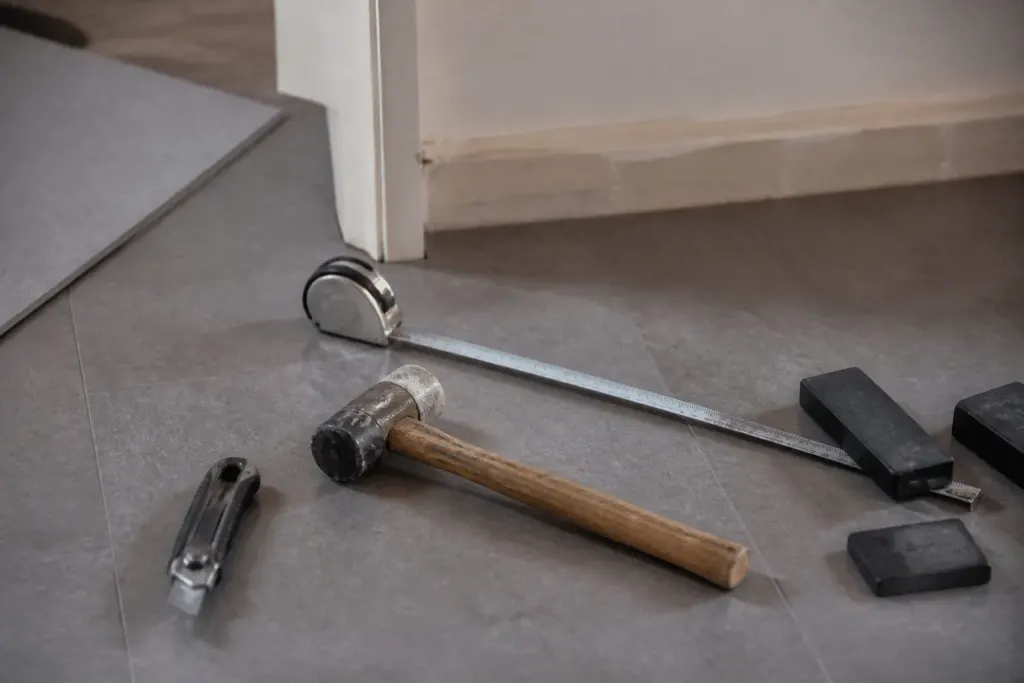 Mètre, cutter, maillet et cales sur dalles PVC grises