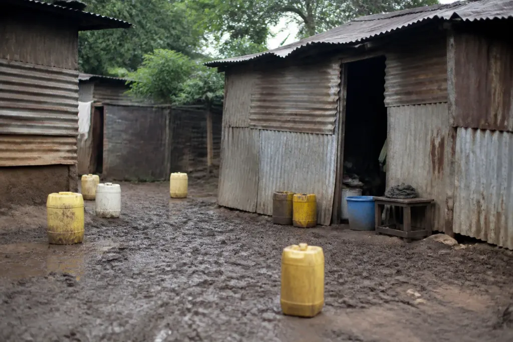 Cabanes en tole sur sol boueux avec bidons plastique