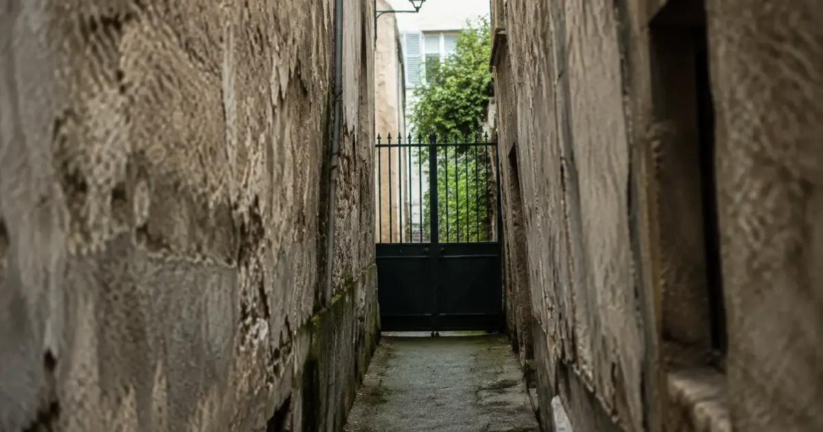 Ruelle etroite aux murs uses et barriere metallique fermee