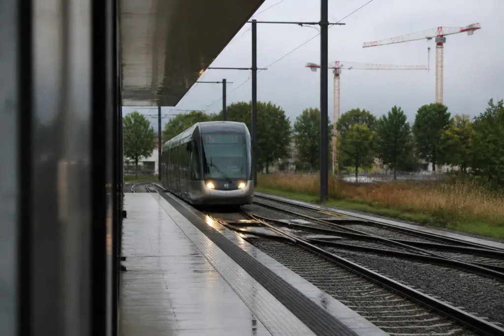 Tramway arrivant en gare, grues de chantier au loin